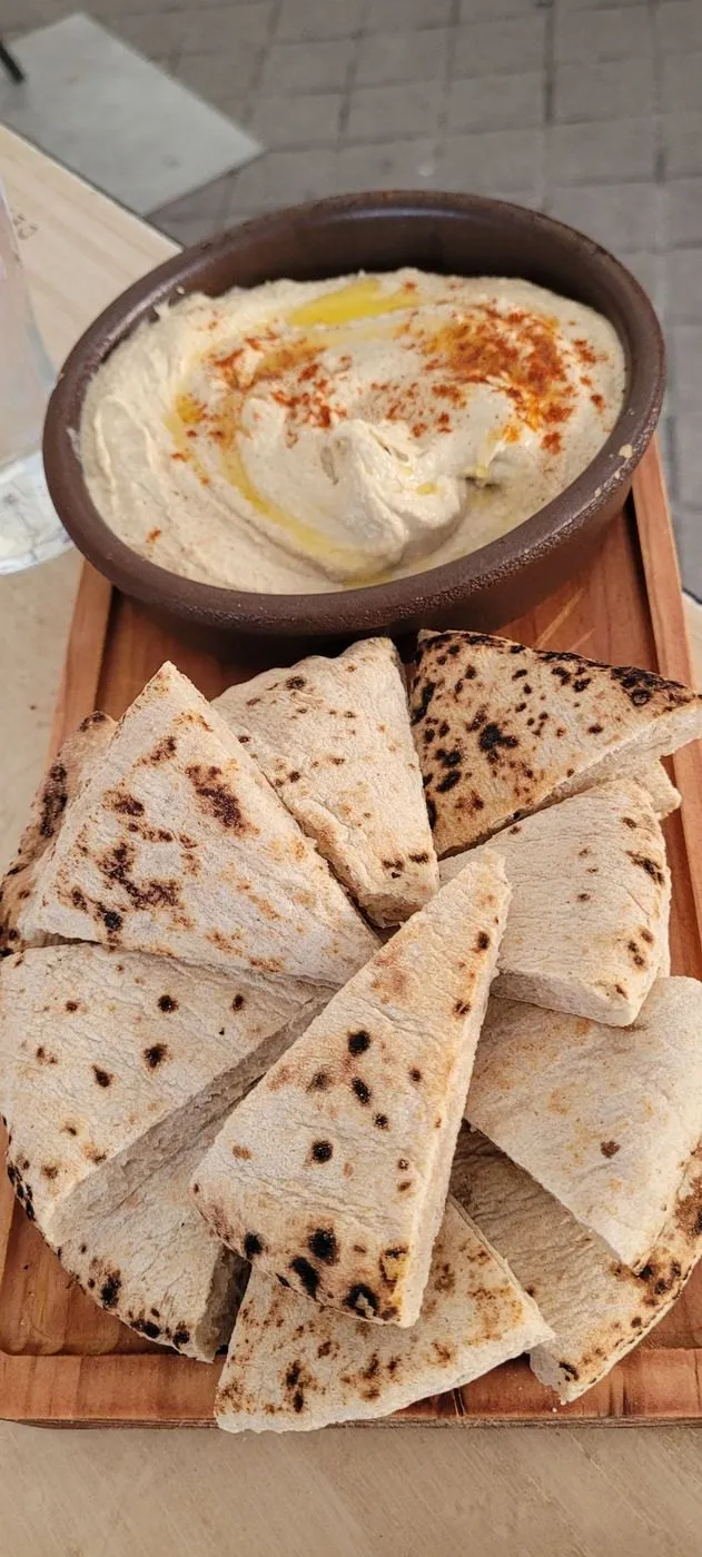 Hummus con pimentón y aceite en un cuenco, con pan de pita en una tabla
